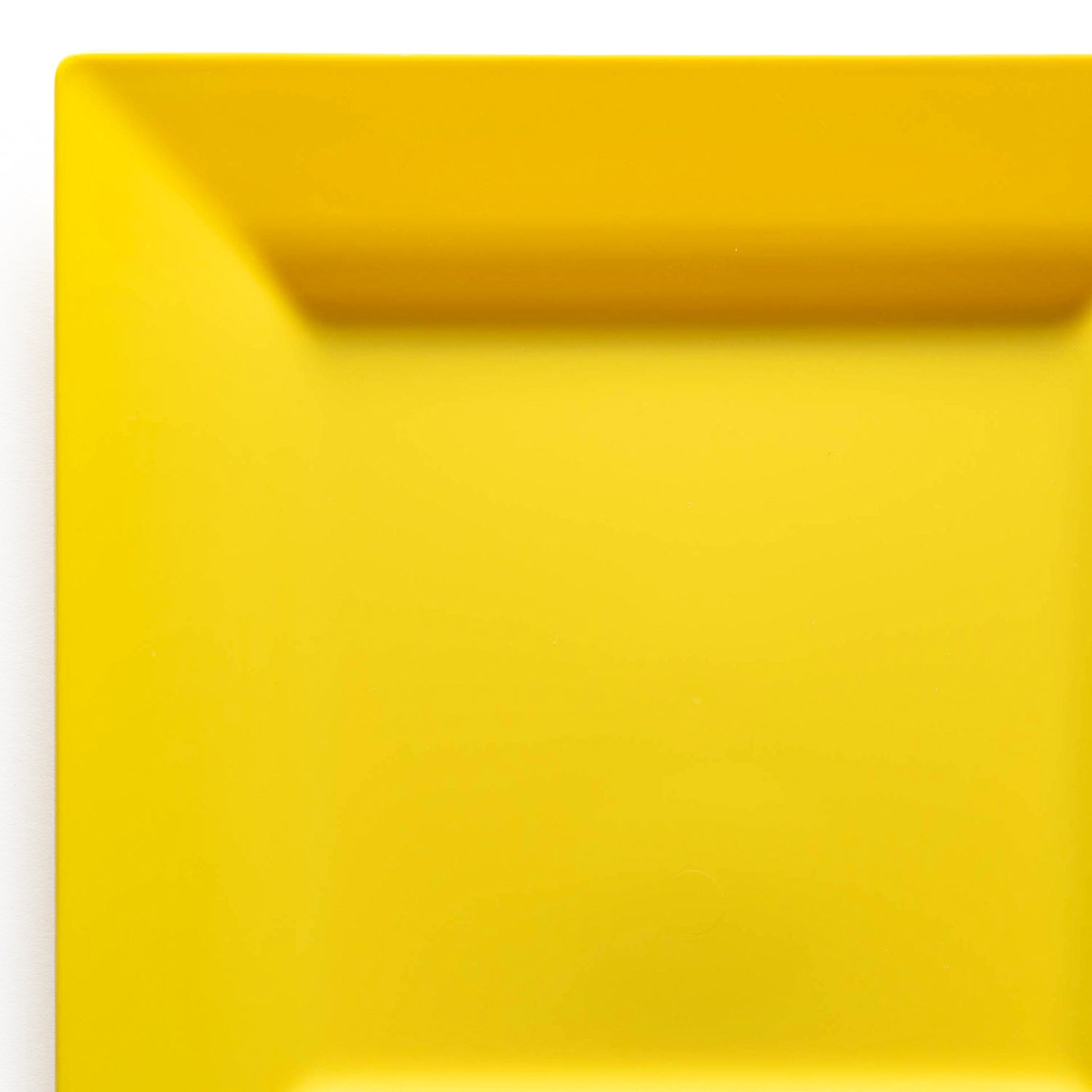A close-up image of a bright yellow Yellow Square Disposable Plastic Dinner Plate (9.5") with a slightly raised rim. The plate has clean lines and a smooth surface, photographed against a plain white background. Only part of the plate is visible, occupying the top right corner of the image.